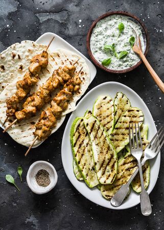 Chicken skewers, grilled zucchini, tortillas and tzadziki sauce - delicious greek style lunch on a dark background, top viewの写真素材