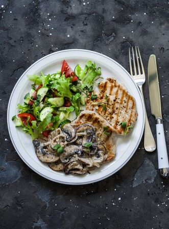 Balanced food - grilled pork with creamy mushroom sauce and fresh vegetable salad on a dark background, top viewの写真素材