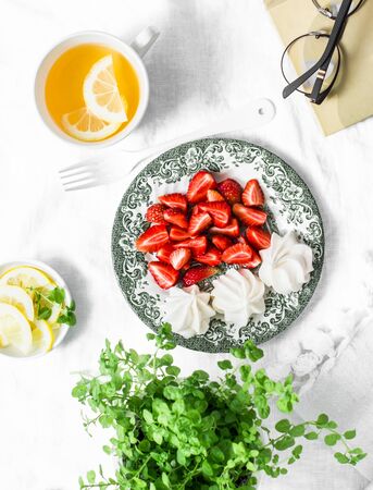 Fresh strawberries, meringue, green tea with lemon, book - cozy home still life on a light background, top viewの写真素材