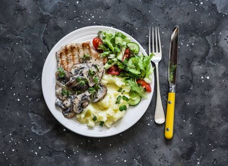 Comfort home cooked food - grilled pork, mashed potatoes with creamy mushroom sauce and fresh vegetable salad on a dark background, top viewの写真素材