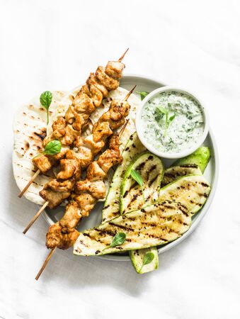 Chicken skewers souvlaki, grilled zucchini, tortillas and tzadziki sauce - delicious greek style lunch on a light background, top viewの写真素材