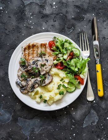 Comfort home cooked food - grilled pork, mashed potatoes with creamy mushroom sauce and fresh vegetable salad on a dark background, top viewの写真素材