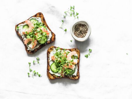 Grilled whole grain bread cream cheese shrimp cucumber micro greens sandwiches on a light background, top viewの写真素材