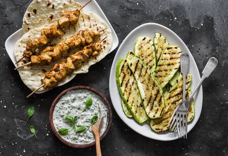 Chicken skewers, grilled zucchini, tortillas and tzadziki sauce - delicious greek style lunch on a dark background, top viewの写真素材