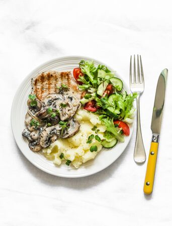 Comfort food - grilled pork chops, mashed potatoes with creamy mushroom sauce and fresh vegetable salad on a light background, top viewの写真素材