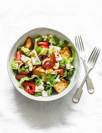 Simple salad with fresh tomatoes, crispy ciabatta, mozzarella cheese, green salad with olive oil, mustard, lemon dressing on a light background, top viewの写真素材