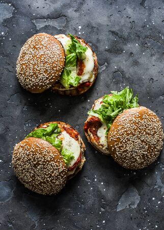Homemade whole grain bun, grilled chicken patty, tomato sauce, mozzarella cheese burgers on a dark background, top viewの写真素材
