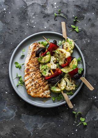 Grilled pork chops, vegetables skewers and naan flatbread on a dark background, top viewの写真素材