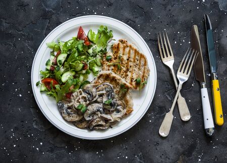 Grilled pork chops with creamy mushroom and fresh tomato, cucumber, greens salad on a dark background, top viewの写真素材