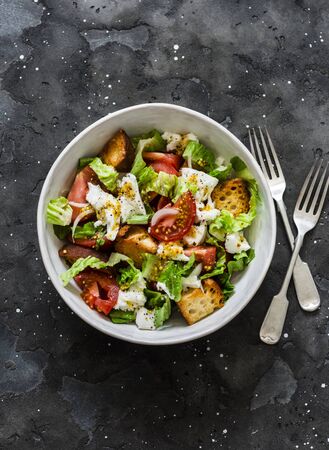 Simple rustic italian salad with fresh tomatoes, ciabatta bread, mozzarella cheese, green salad with olive oil on a dark background, top viewの写真素材