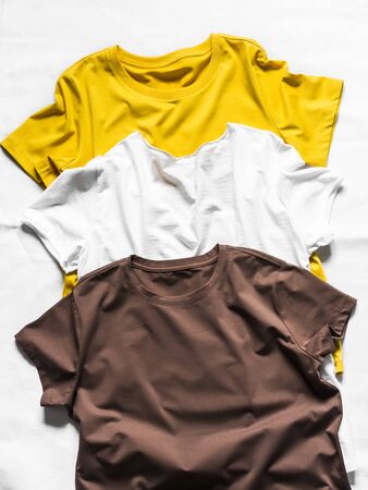 Basic cotton t-shirts. White, yellow, brown women's t-shirts on a light background, top viewの写真素材