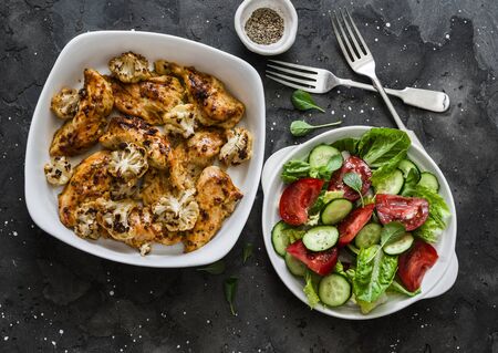 Mustard baked chicken fillet with cauliflower and fresh vegetable salad on a dark background, top viewの写真素材