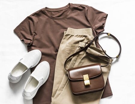 Brown t-shirt, cotton joggers, white sneakers, leather cross body bag on a light background, top view. Fashion beauty conceptの写真素材