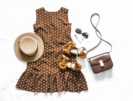 Summer brown polka dot sleeveless dress, suede sandals, leather crossbody bag, sunglasses and hat on a light background, top viewの写真素材