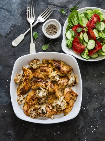 Roasted chicken fillet with cauliflower and fresh tomatoes, cucumbers salad on a dark background, top viewの写真素材