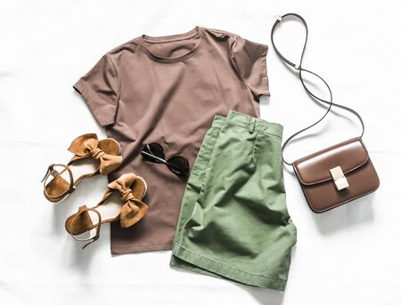 Women's summer clothing-brown t-shirt, cotton green shorts, suede sandals, cross body bag on a light background, top view. Fashion beauty conceptの写真素材
