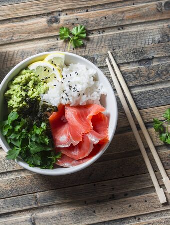 Salmon poke bowl on wooden background, top view. Rice, avocado puree, salmon, seaweed - healthy food concept asian styleの写真素材