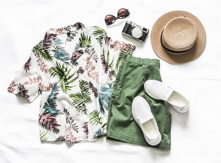 Set of women's clothing for vacation, travel - shirt, cotton shorts, leather sneakers, hat, sunglasses and camera on a light background, top viewの写真素材