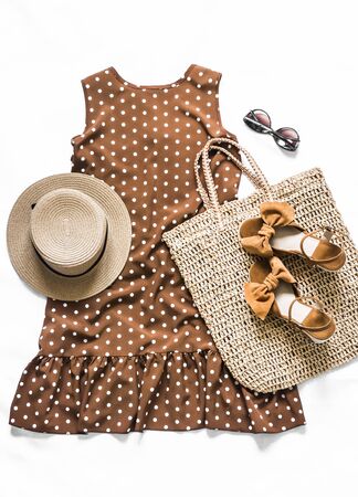 Women's clothing - brown polka dot dress, straw tote bag, suede wedge sandals, sunglasses on a light background, top view. Fashion summer conceptの写真素材