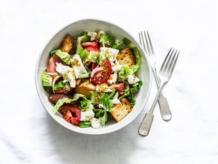Rustic italian salad with fresh tomatoes, crispy ciabatta, mozzarella cheese, green salad with olive oil, mustard, lemon dressing on a light background, top viewの写真素材