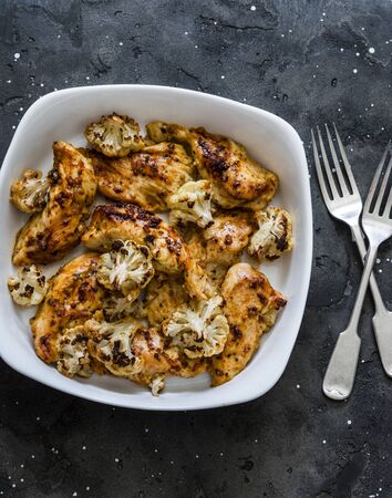 Roasted chicken breast fillets with cauliflower cabbage on a dark background, top view. Delicious lunch, tapas, appetizersの写真素材
