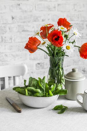 Kitchen still life - fresh spinach in a bowl, bouquet of poppies on the table in a bright room. Cozy interior home still lifeの写真素材