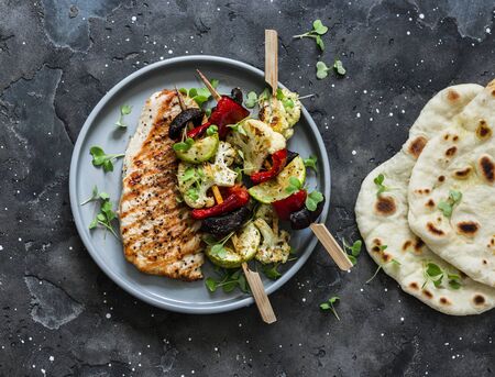 Grilled pork meat chops, vegetables mushrooms, peppers, zucchini skewers and naan flatbread on a dark background, top viewの写真素材