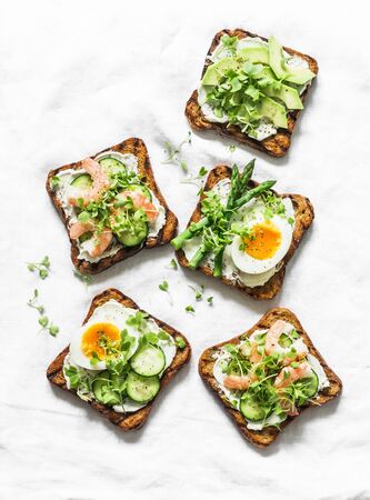 Variety sandwiches with cream cheese, egg, asparagus, avocado, cucumber, shrimp, micro greens on a light background, top view. Delicious tapas, snack, appetizersの写真素材