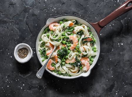 Green peas, prawns, spinach, cream sauce tagliatelle pasta in a cooking skillet  on a dark background, top viewの写真素材