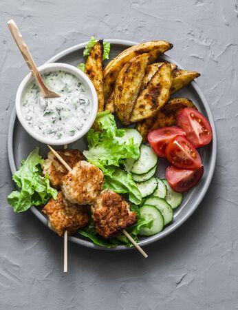 Fish skewers, roasted potatoes, fresh vegetables and tzatziki sauce on grey background, top viewの写真素材