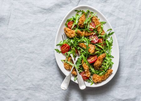 Deep-fried chicken fingers, rockets, cherry tomatoes salad on a grey background, top view. Delicious  snack,  appetizer, tapasの写真素材