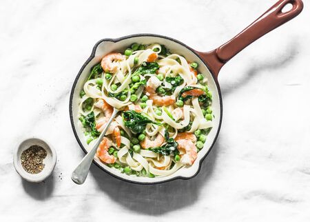 Italian pasta with green peas, shrimps, spinach, cream sauce tagliatelle in a cooking skillet  on a light background, top viewの写真素材