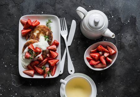 Delicious breakfast - cottage cheese fritters with strawberry and green tea on a dark background, top viewの写真素材