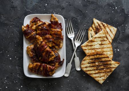 Delicious tapas - baked chicken breast wrapped in bacon, grilled bread on a dark background, top viewの写真素材
