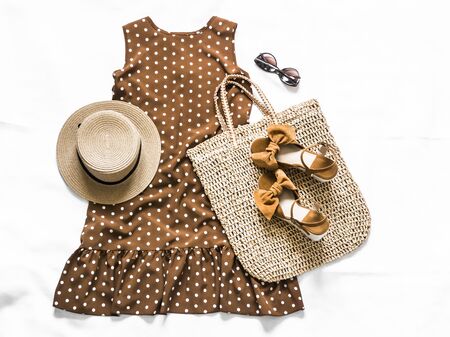 Women's summer clothing - brown polka dot dress, straw tote bag, suede wedge sandals, sunglasses on a light background, top view. Fashion conceptの写真素材