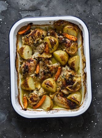 Chicken with new potatoes, carrots, lemon and thyme in baking tray on a dark background, top viewの写真素材