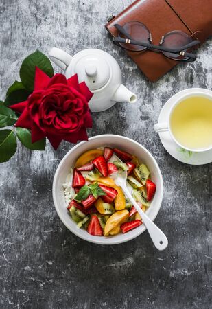 Delicious breakfast. Cottage cheese with natural yogurt, strawberries, kiwi, apricots, green tea and personal planner organizer on a gray background, top viewの写真素材