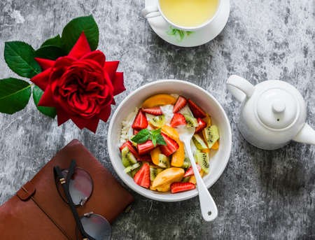 Delicious breakfast still life. Cottage cheese with natural yogurt, strawberries, kiwi, apricots, green tea and personal planner organizer on a gray background, top viewの写真素材
