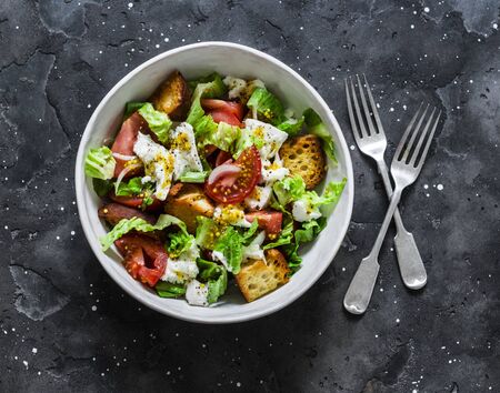 Simple rustic italian salad with fresh tomatoes, ciabatta crunchy bread, mozzarella cheese, green salad  on a dark background, top viewの写真素材