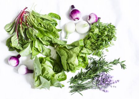Fresh herbs and vegetables on a white background, top view. Spinach, coriander, romaine salad, lavender, onion - delicious flavorful food ingredientsの写真素材