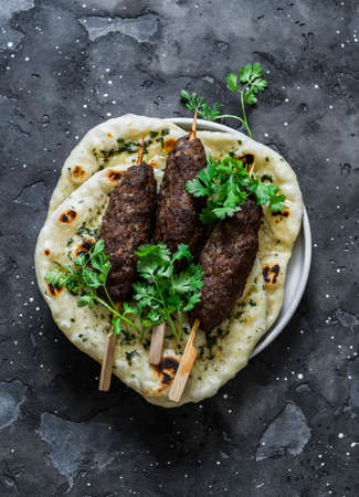 Grilled lamb kebab and flatbreads with garlic and herbs on a dark background, top viewの写真素材