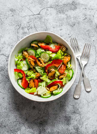 Seafood and vegetables salad. Salad with tomatoes, cucumbers, bell peppers and canned mussels on a gray background, top viewの写真素材
