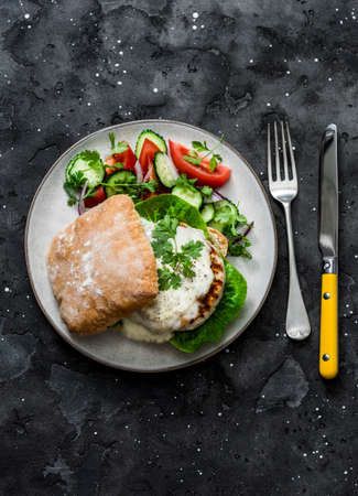 Ciabatta bread sandwich burger with chicken cutlet and mayonnaise mustard sauce and vegetables salad on a dark background, top viewの写真素材