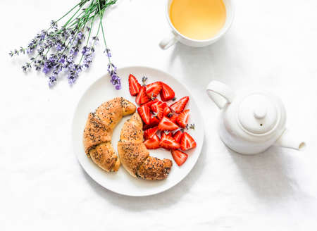Breakfast morning still life. Homemade poppy seeds croissants, strawberries, green tea, bunch of lavender on a light background, top viewの写真素材