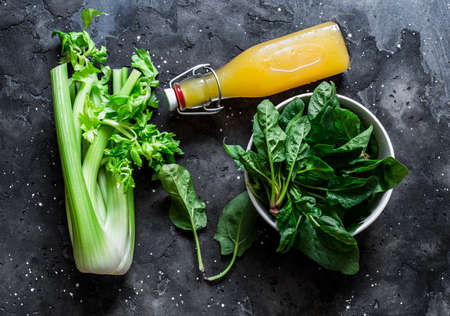 Ingredients for detox diet green smoothies - fresh celery, spinach, natural orange juice on a dark background, top view. Healthy drinkの写真素材