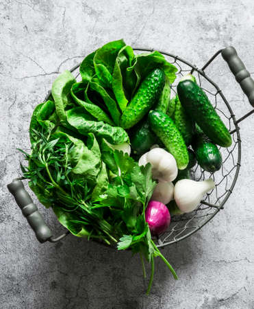 Fresh vegetables cucumbers, romaine lettuce, onions, herbs in a metal vintage basket on a gray background, top view. Food ingredientsの写真素材