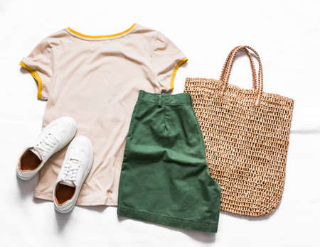 Women's cotton bermuda shorts, t-shirt, straw tote bag, white leather sneakers on a light background, top view. Fashion conceptの写真素材
