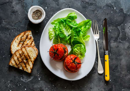 Delicious appetizer, tapas - stuffed ground beef tomatoes, romano salad, grilled bread on a dark background, top viewの写真素材
