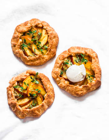Ripe peaches, fresh thyme mini pies with cream ice cream - delicious summer dessert on a light background, top viewの写真素材