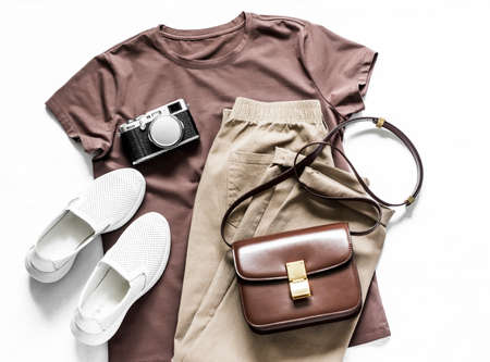 Women clothing. Brown t-shirt, cotton joggers jeans, white sneakers, leather cross body bag and camera on a light background, top view. Fashion conceptの写真素材